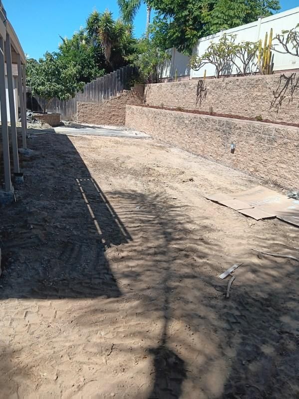 Dirt yard with retaining walls and partial construction under a blue sky.