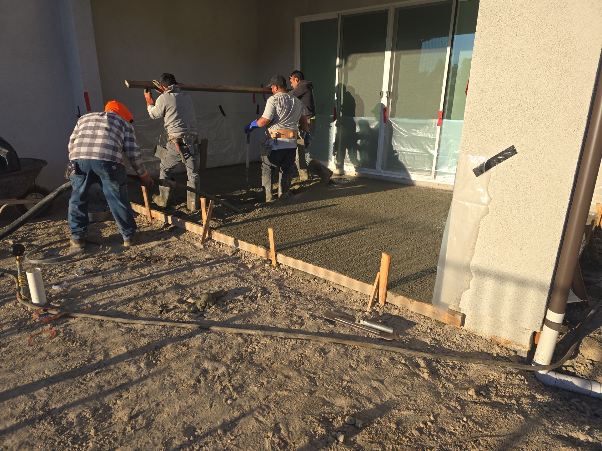Workers pouring concrete for a patio. Sunlight, outdoor setting, framed with wood, leveled.