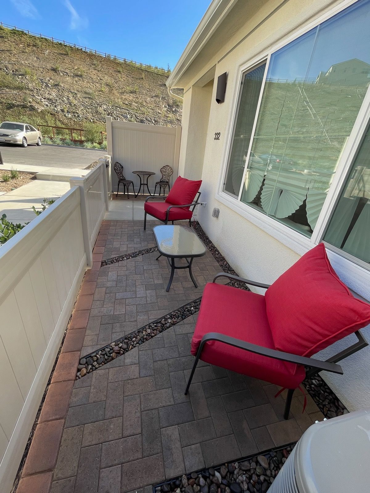 Outdoor patio with red chairs, small table, and brick paving, beside a building with a large window and a view of a mountain.