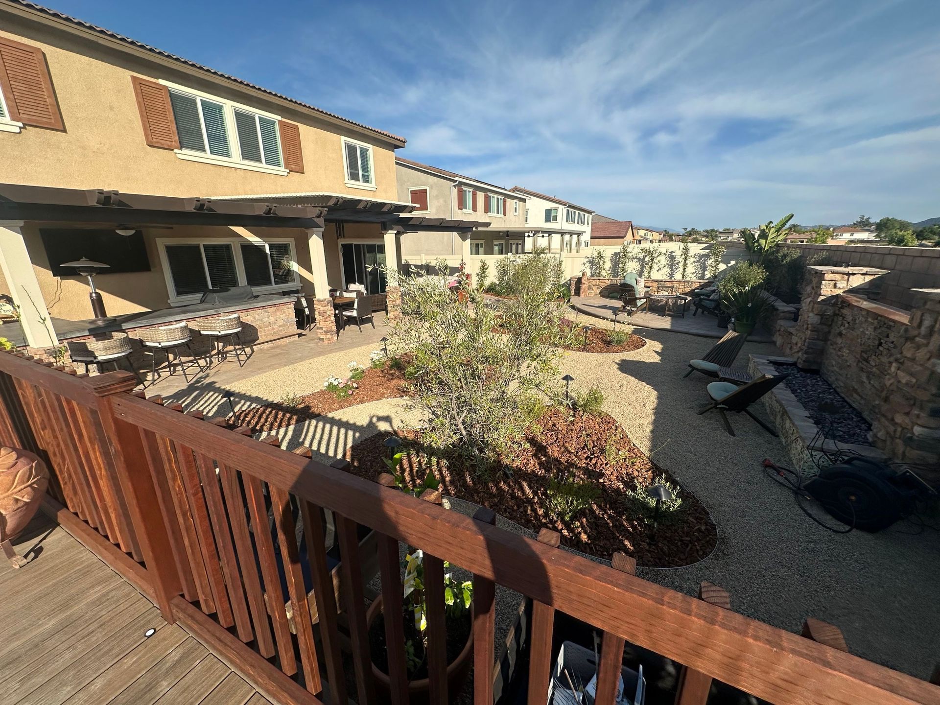 Backyard patio with townhouse homes, wooden deck railing, and gravel courtyard under a bright blue sky