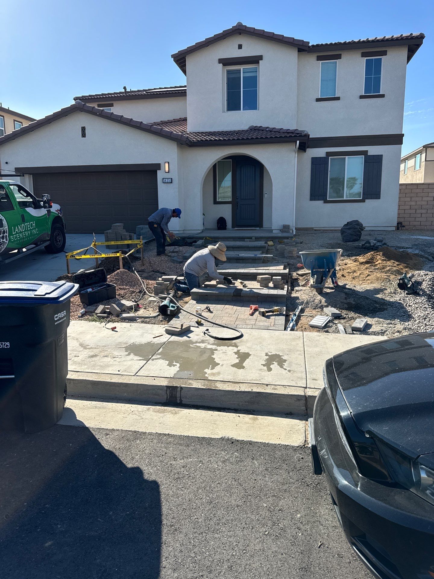 Workers excavating the front yard of a two-story house.  A truck and a car are parked nearby.