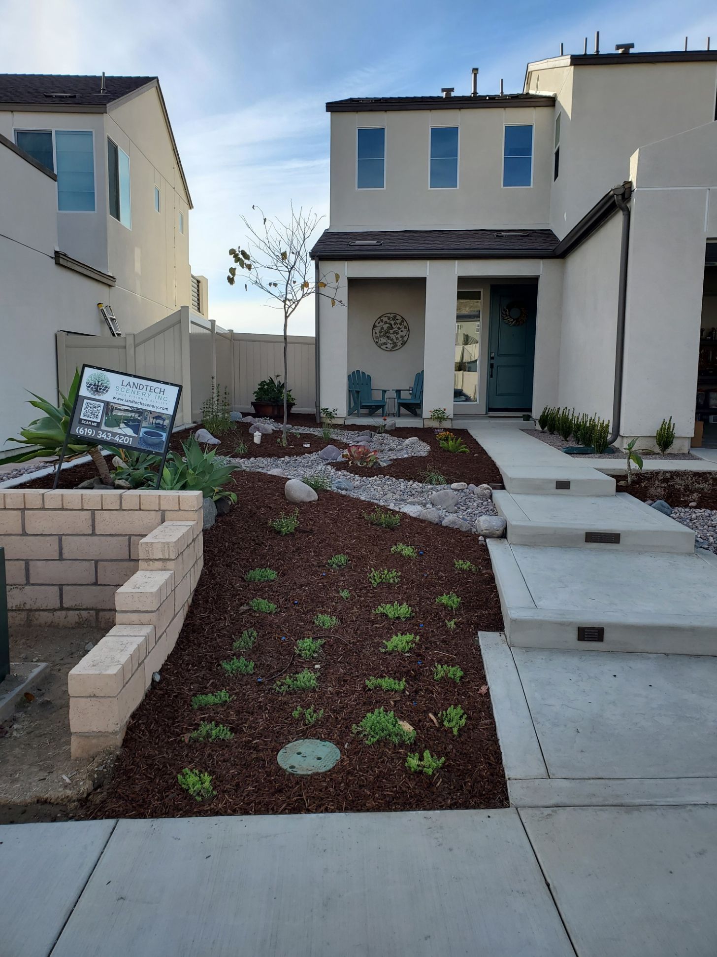 Front yard of a two-story beige house with drought-tolerant landscaping and a concrete walkway.
