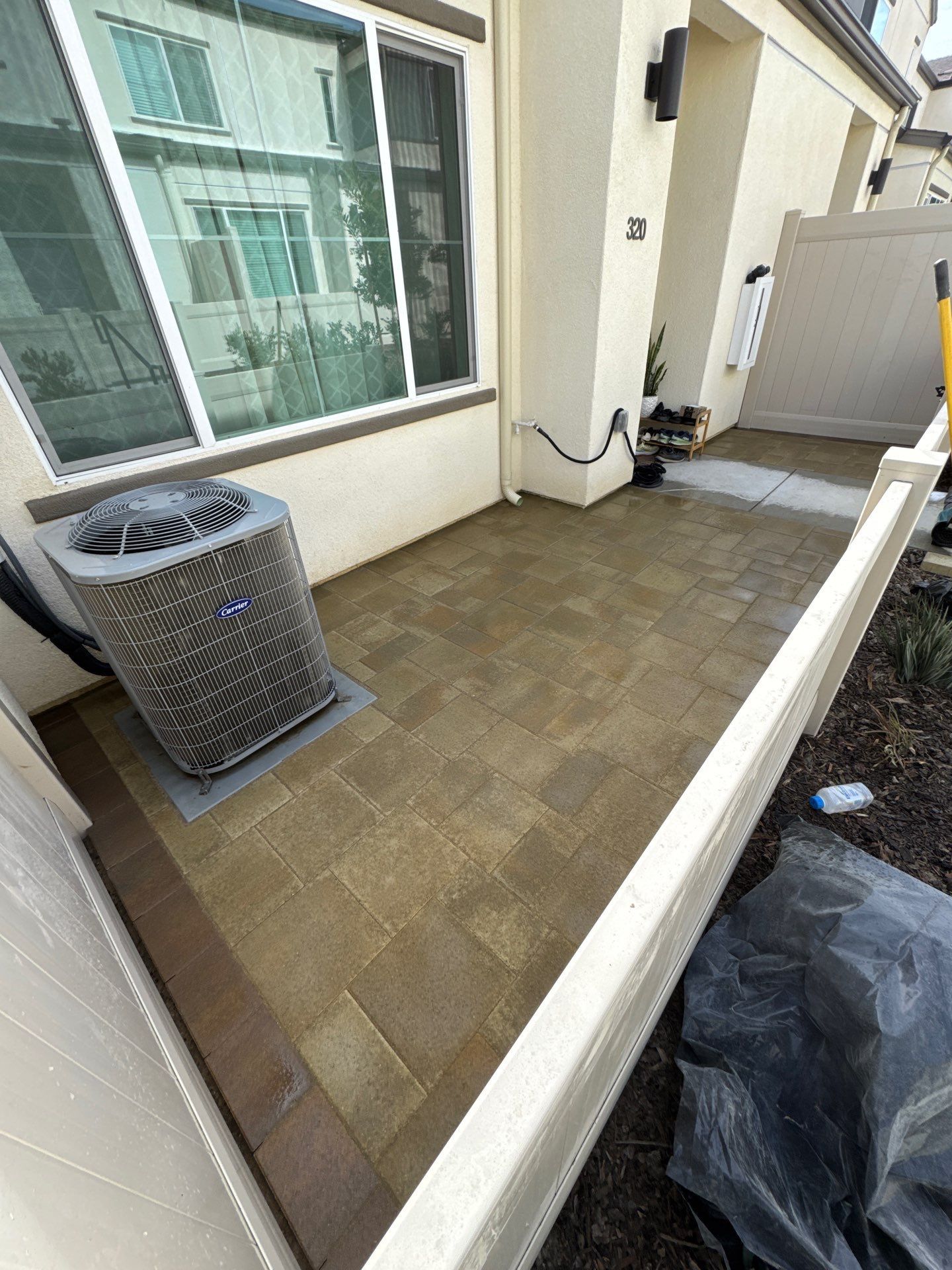 Patio with brown pavers, air conditioning unit, sliding glass door, and a white fence.