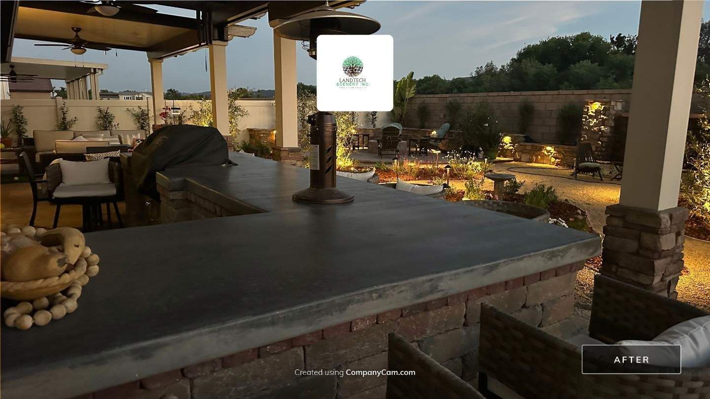 Outdoor patio with a stone bar, covered seating, and a lit garden at dusk