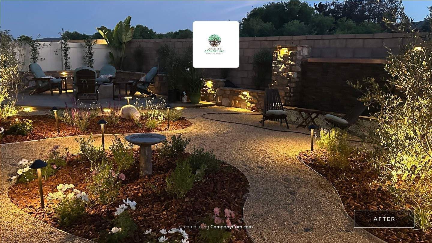 Illuminated garden patio with winding gravel path, potted plants, stone seating, and warm lights at dusk