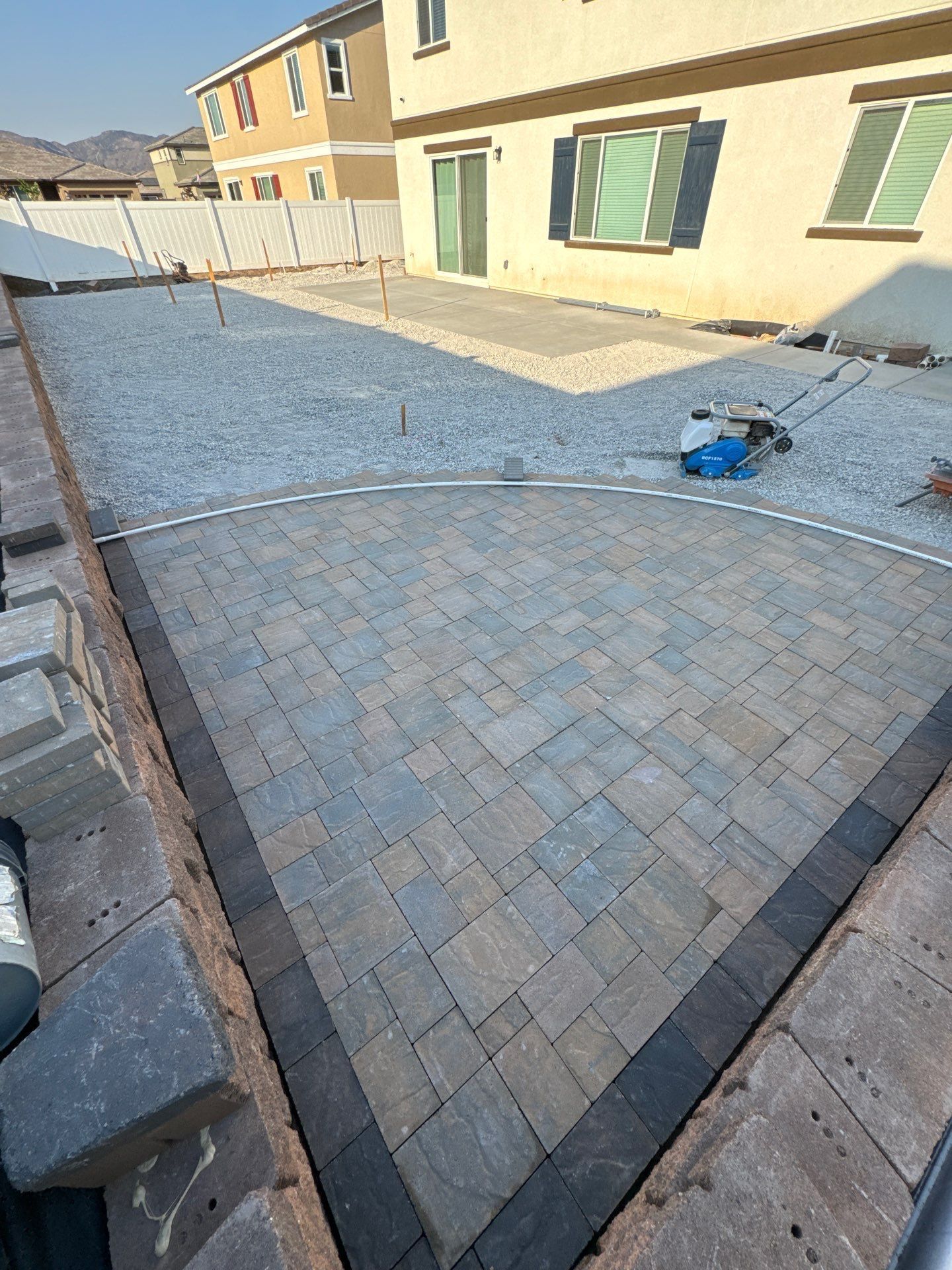 Patio construction: paving stones laid with gray gravel background. A house is visible.