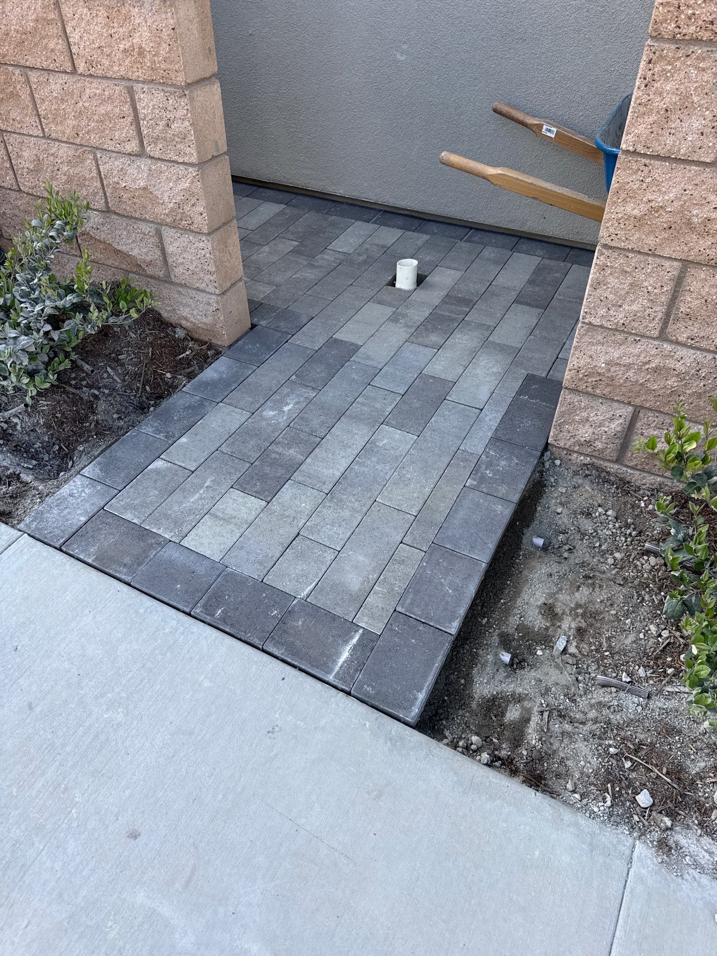 Paver walkway with dark border, leading to a recessed area with a white pipe.