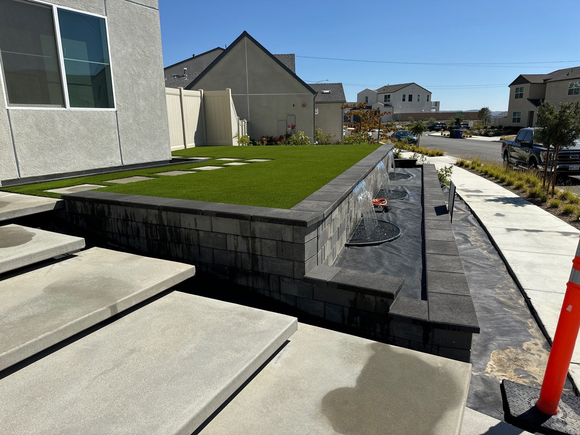 Exterior view: Modern home with retaining wall, artificial grass, and water feature. Sunny day.