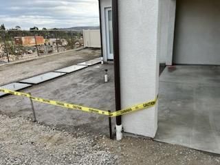 Construction site: Concrete patio with caution tape, gutter, and building in background. Cloudy sky.