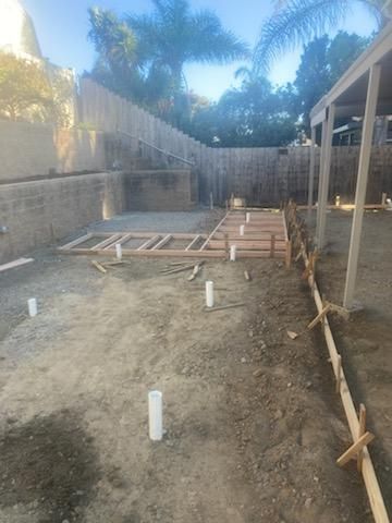 Construction site: wooden frames, concrete forms, and plumbing pipes set in dirt, ready for a build.
