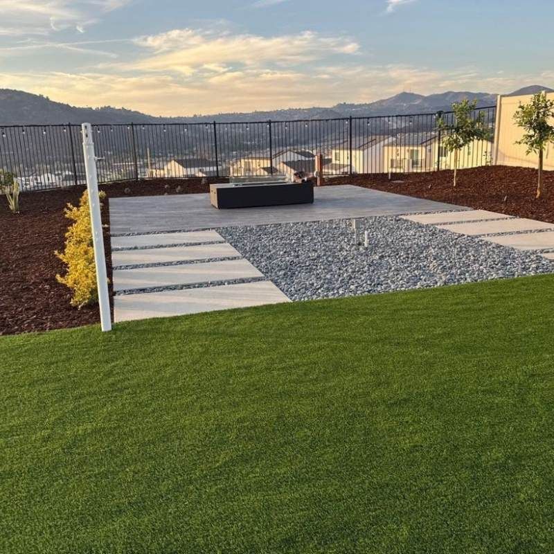 Backyard patio with fire pit, gravel, stepping stones, and green lawn; mountain view.
