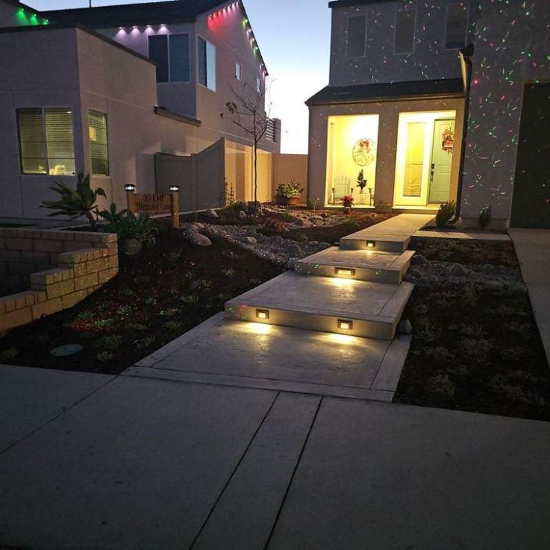 Night view of a house with illuminated steps, landscape, and doorway. Christmas lights are visible.