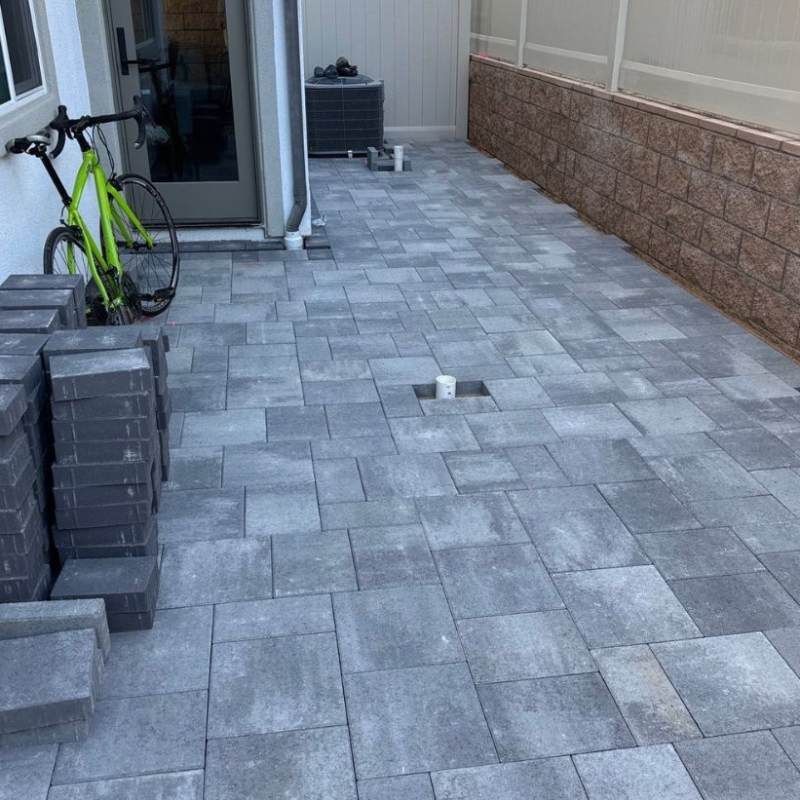 Finished patio paved with gray pavers, with a stack of unused pavers and a bike.