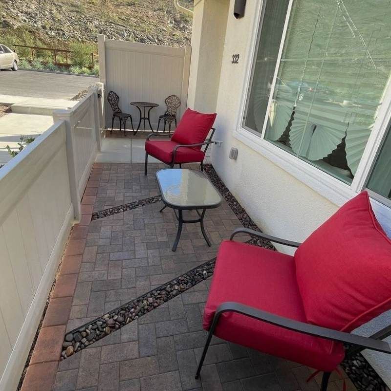 A small patio with red cushioned chairs, a glass-topped table, and a brick pathway.
