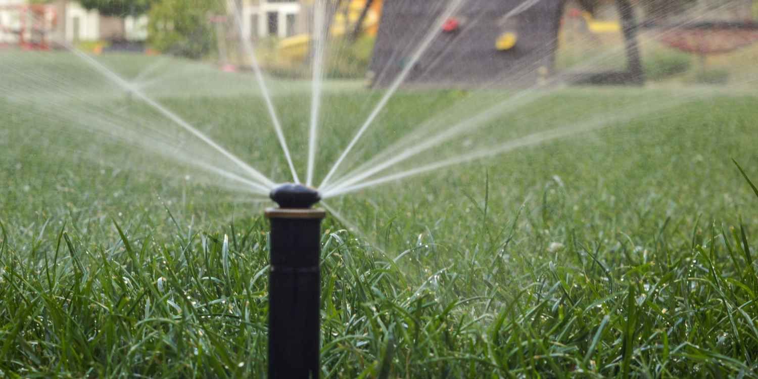 Garden sprinkler spraying water over a green lawn with houses in the background