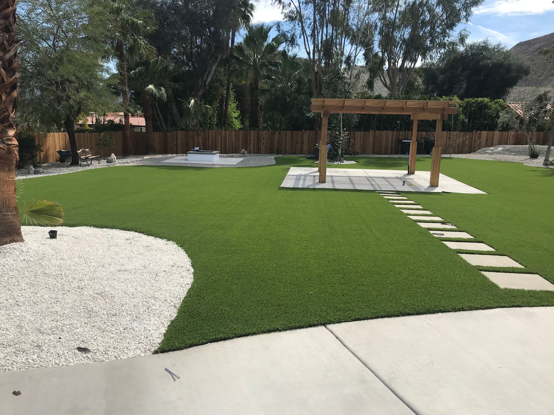 Backyard with green turf, white gravel, wooden pergola, and stepping stones.