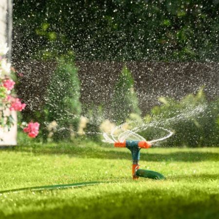 Garden sprinkler spraying water over a green lawn with flowers in the background