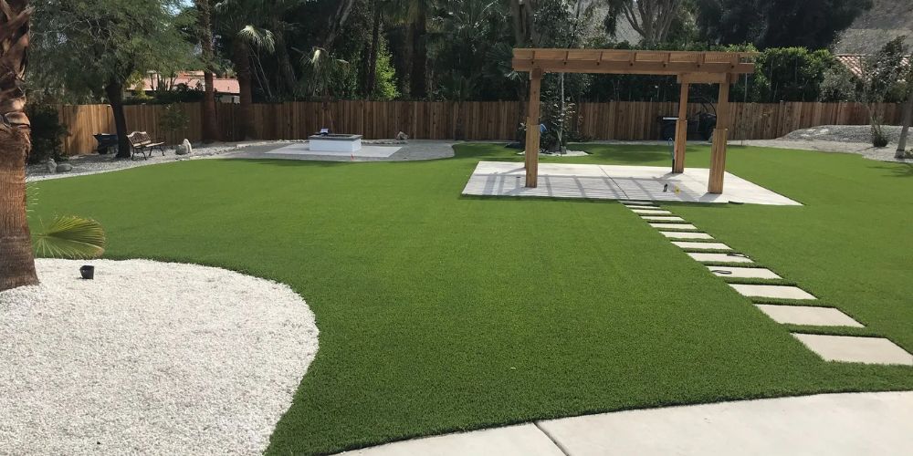 Modern backyard with artificial grass, stone stepping path, pool, and wooden pergola under trees