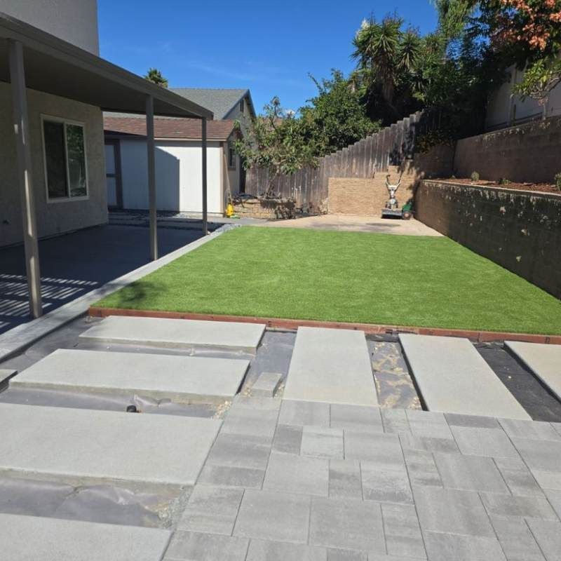 Backyard with stone patio, green turf, and house.