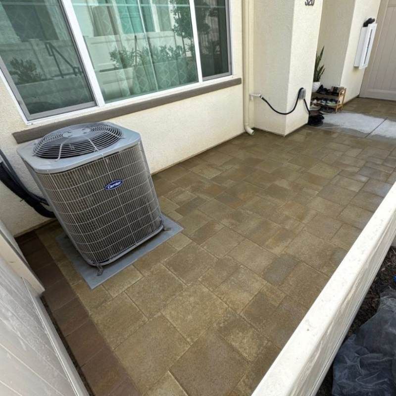 Air conditioning unit on a tiled patio next to a window and house entrance.