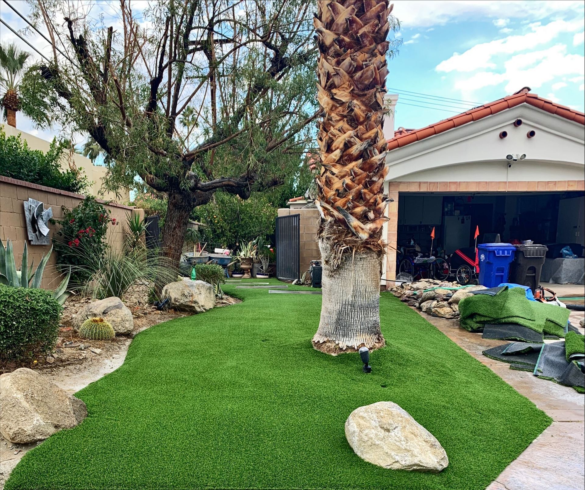 Backyard with artificial green turf, large rocks, and a palm tree in front of a house.