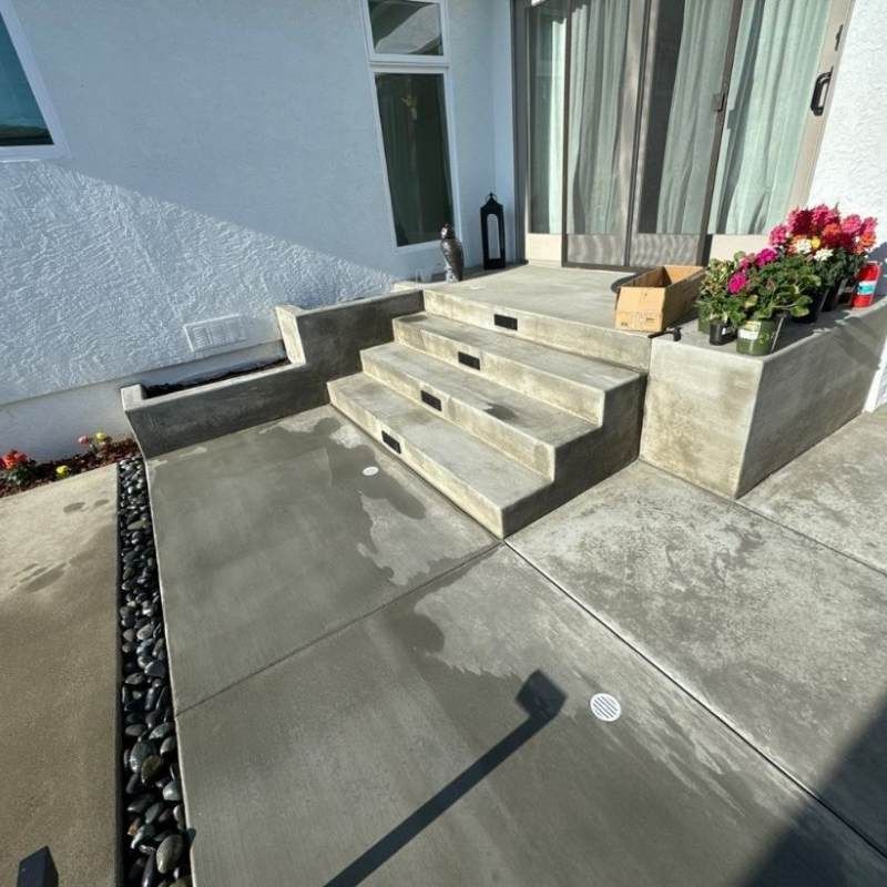 Concrete steps and walkway leading to a modern building entrance. Black stones line the edge.