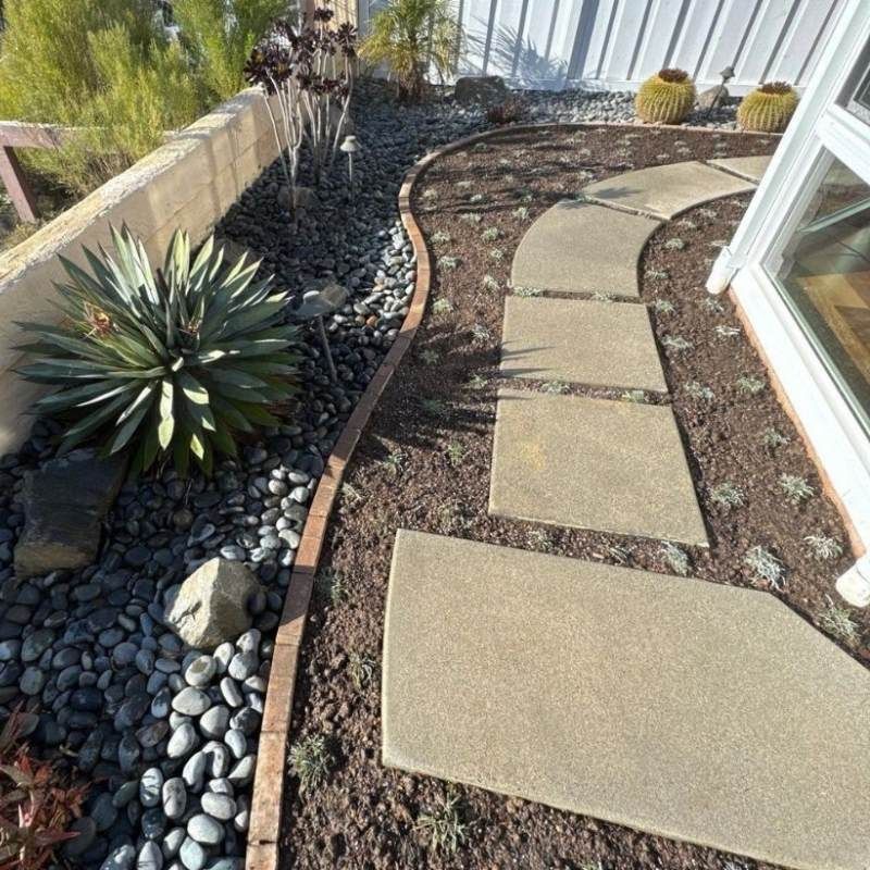 A curving garden path made of stone slabs winds through a bed of dark pebbles and mulch.