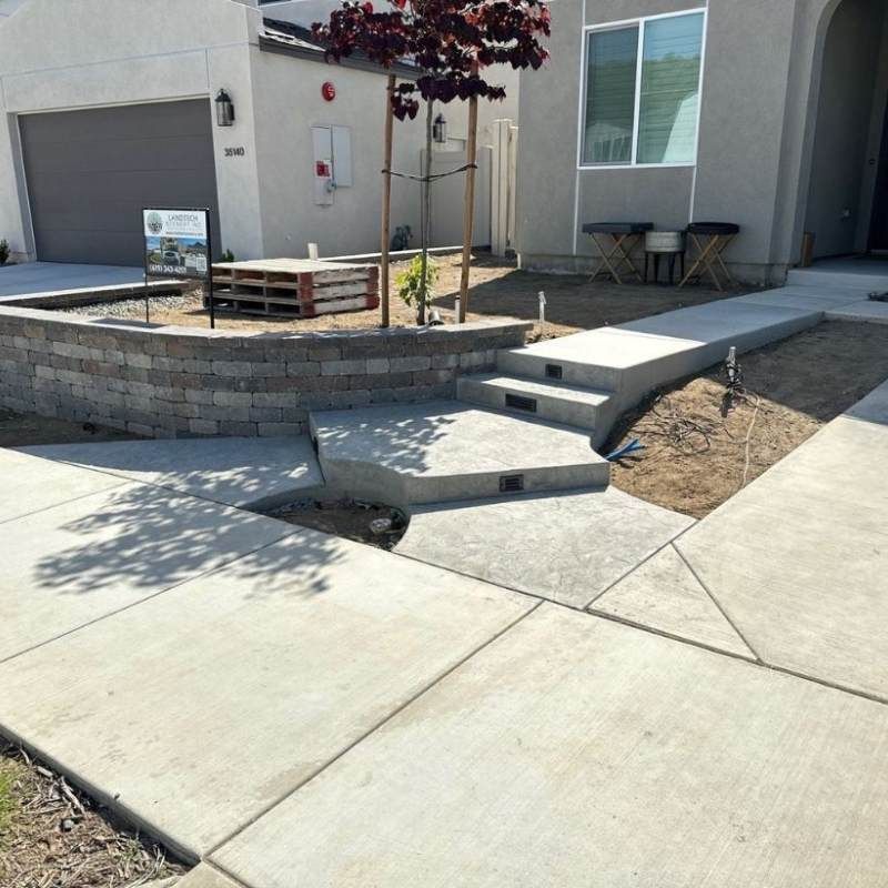 Concrete steps and pathway leading up to a beige house with a retaining wall and small tree.
