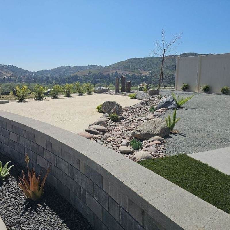 Landscaped yard with retaining wall, rock features, drought-tolerant plants, and a scenic view of hills.