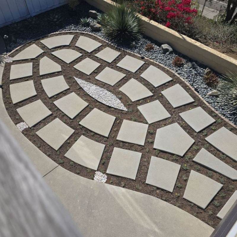 Stone patio with a unique tile pattern surrounded by dirt and landscaping.