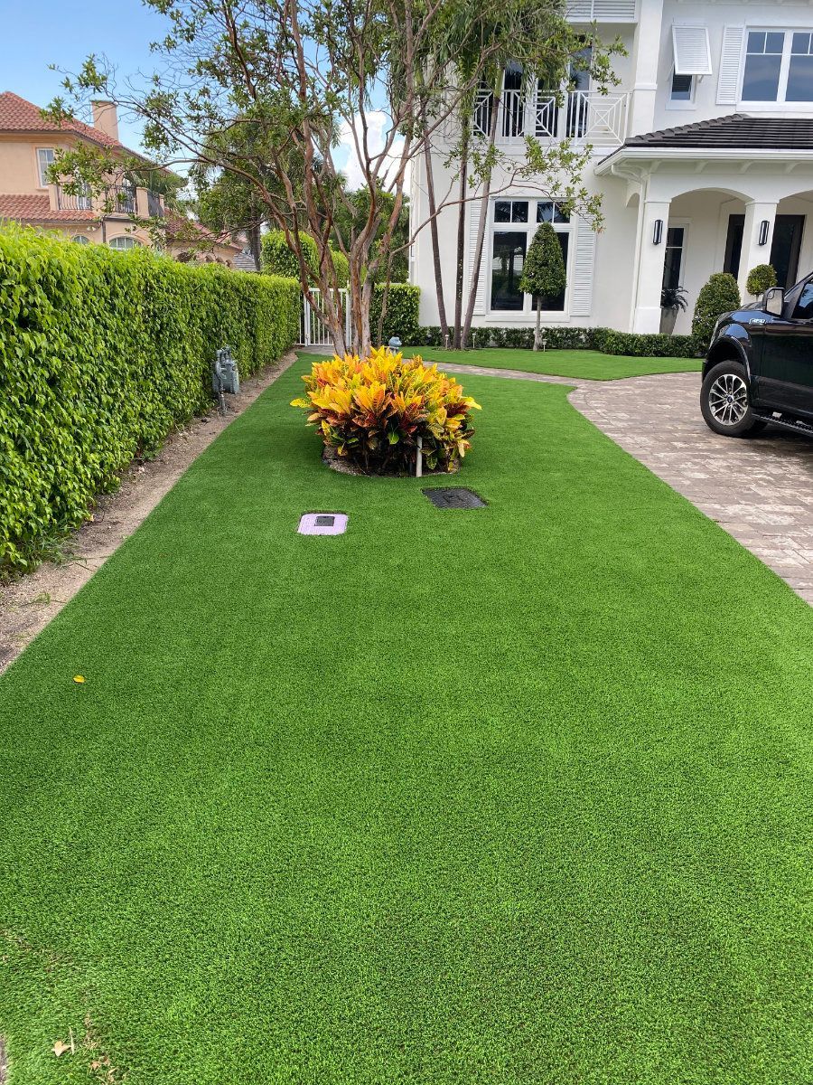 Green artificial turf driveway in front of a white house with landscaping.