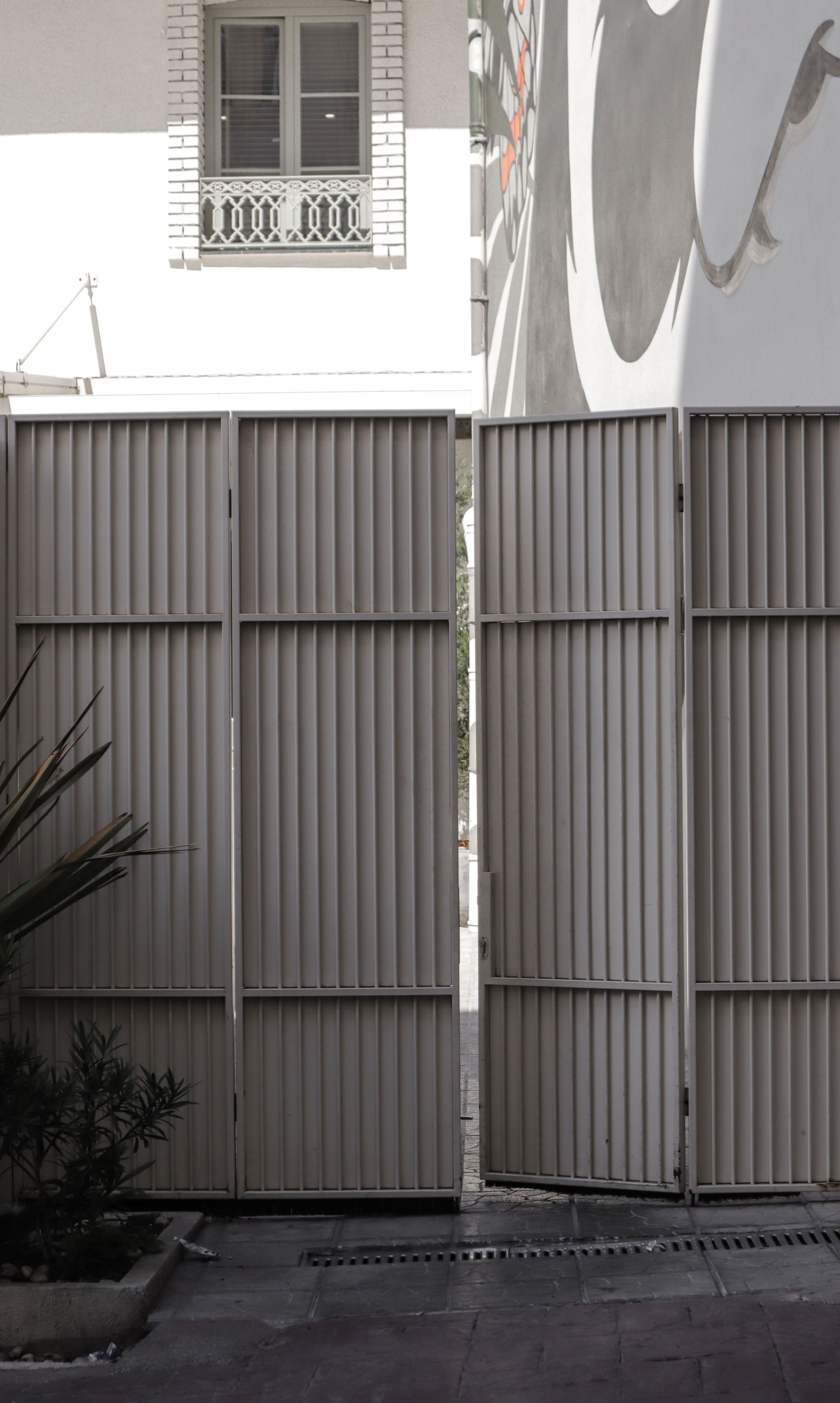Tall gray metal gate beneath a white building facade with a small window and balcony above.