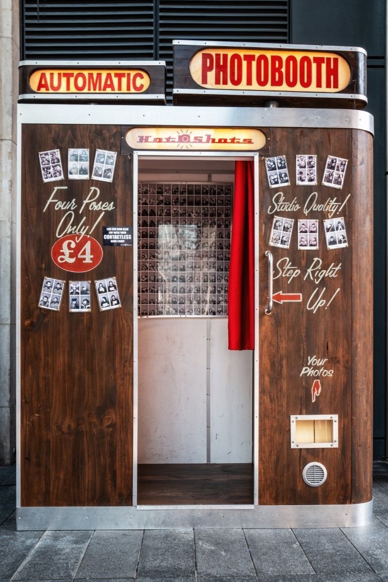 Vintage automatic photobooth with wooden doors and red signage in a street storefront