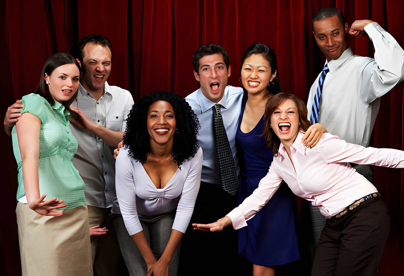 Six smiling coworkers pose together against a red background, leaning in playfully.