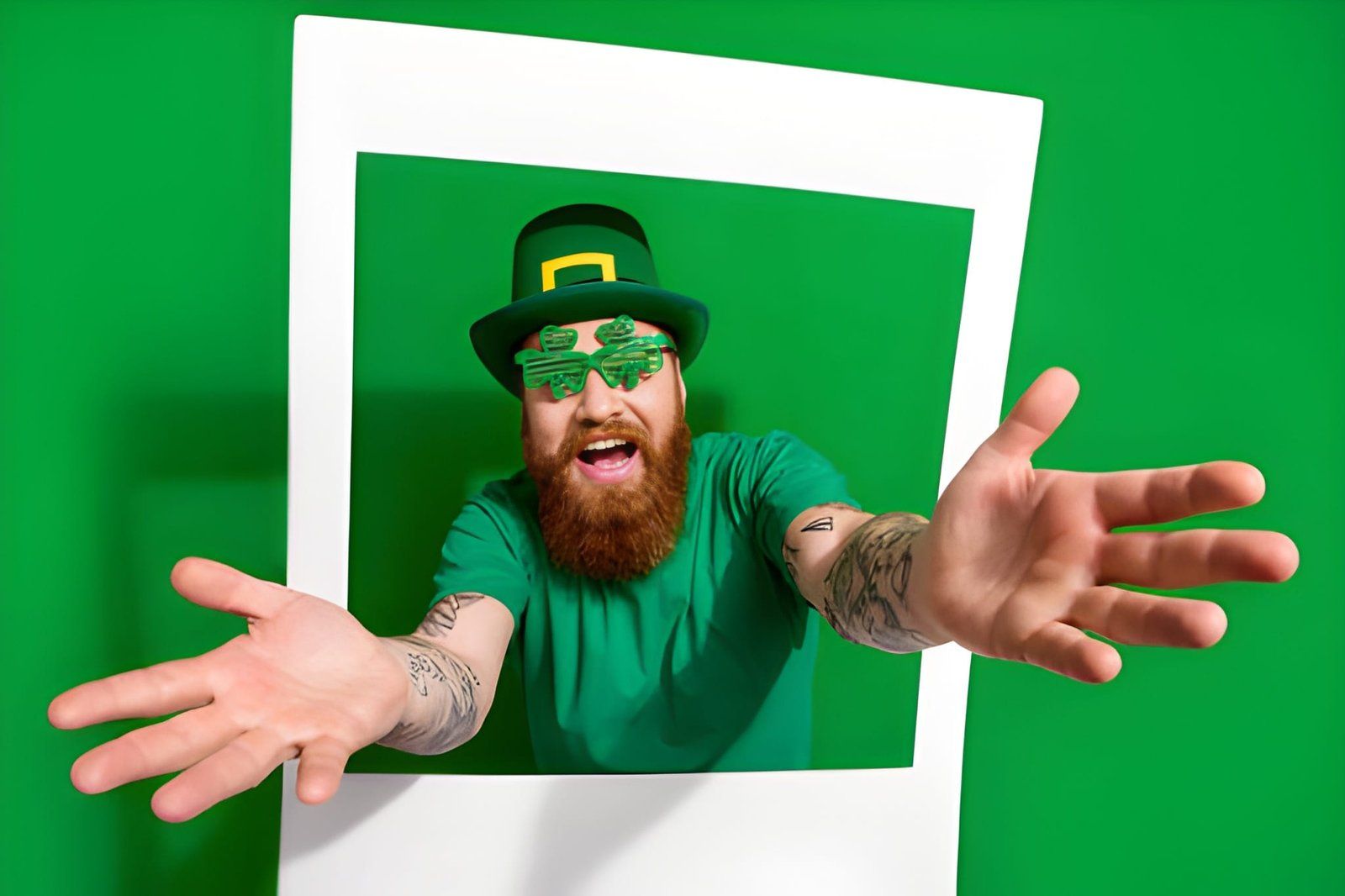 Smiling man in green leprechaun outfit reaching through a tilted white frame on a green background