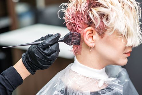 Stylist applying pink hair dye with a brush to a client’s short blonde hair in a salon
