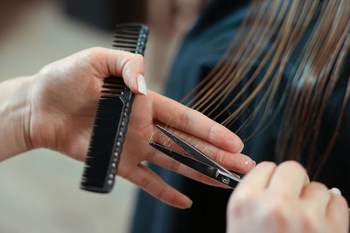 Hands cutting long brown hair with a comb in a salon close-up