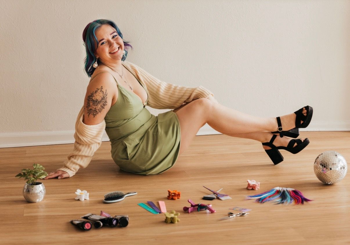Person sitting on a wooden floor with colorful art supplies and toys, smiling in a cozy room