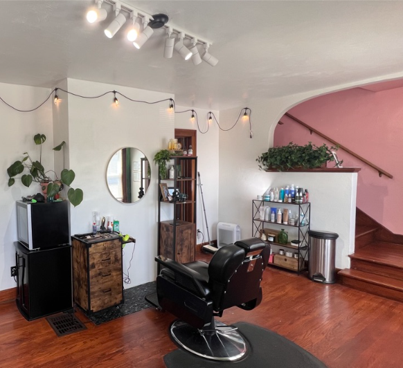 Salon interior with black styling chair, mirrors, plants, and pink staircase wall