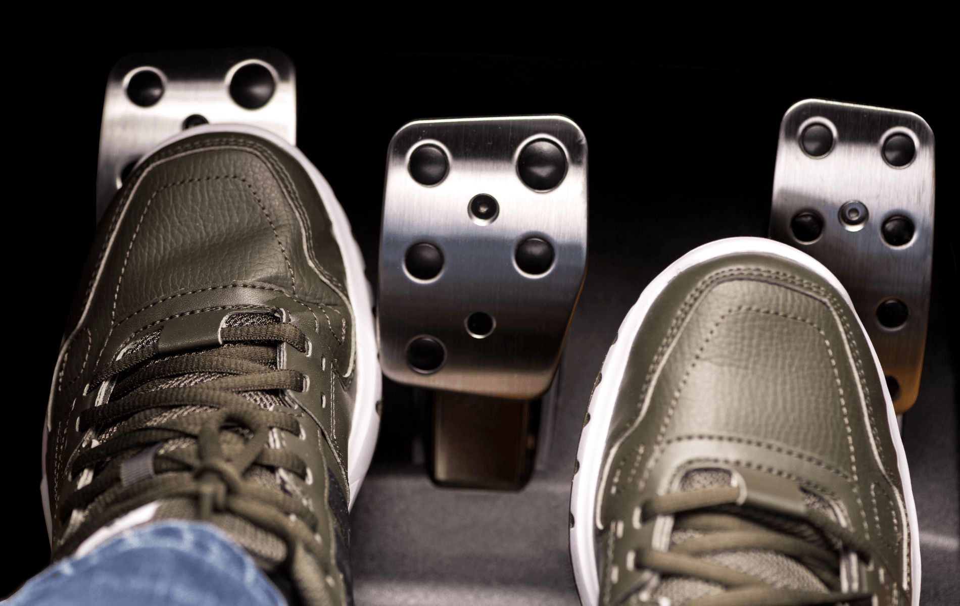 Feet on car pedals, with a black shoe on the left and a gray shoe on the right.