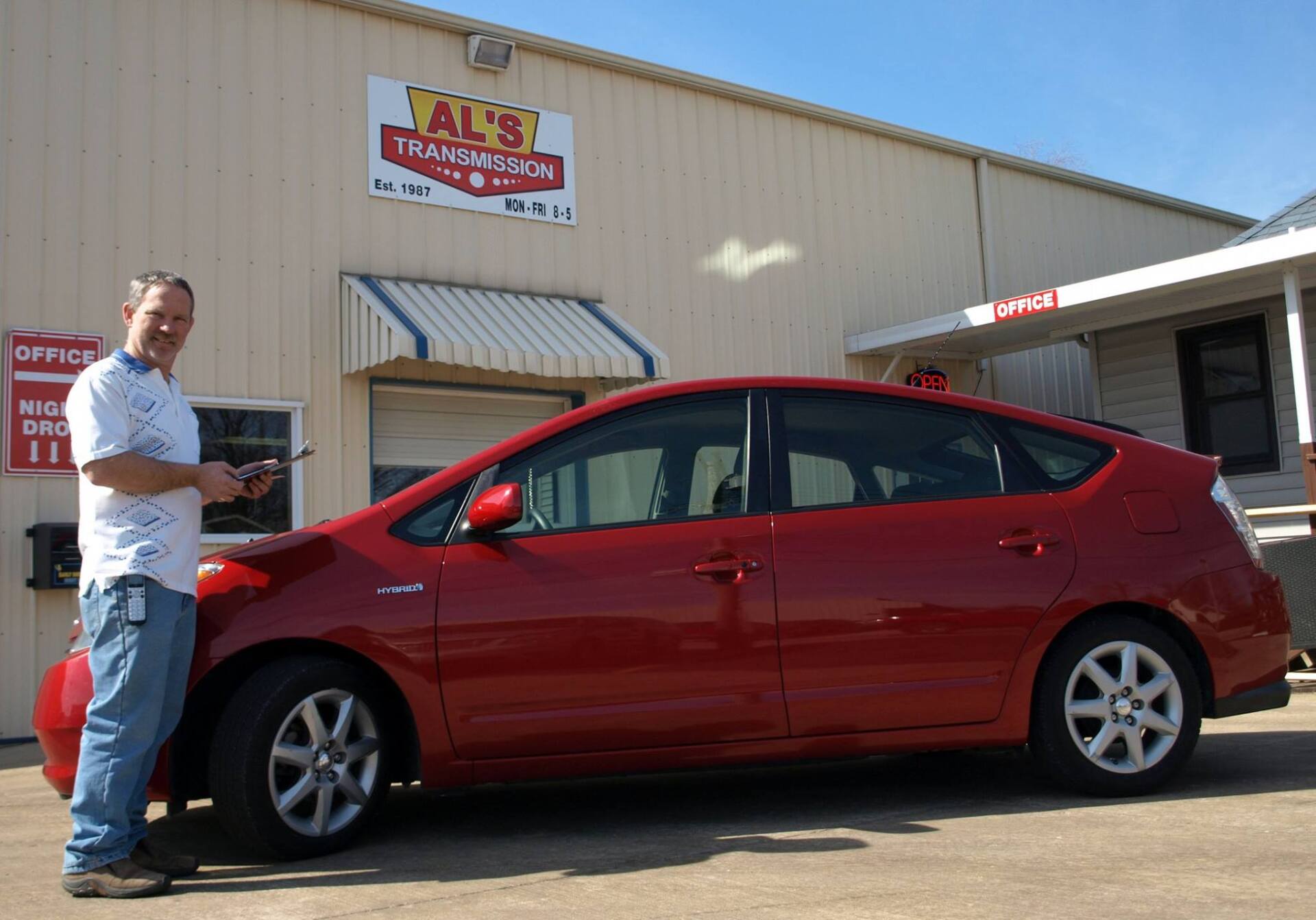 Man standing beside a red sedan outside a shop building