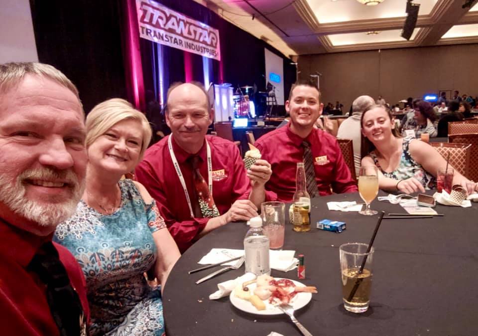 Five people smiling at a banquet table with drinks and desserts in a hotel conference room