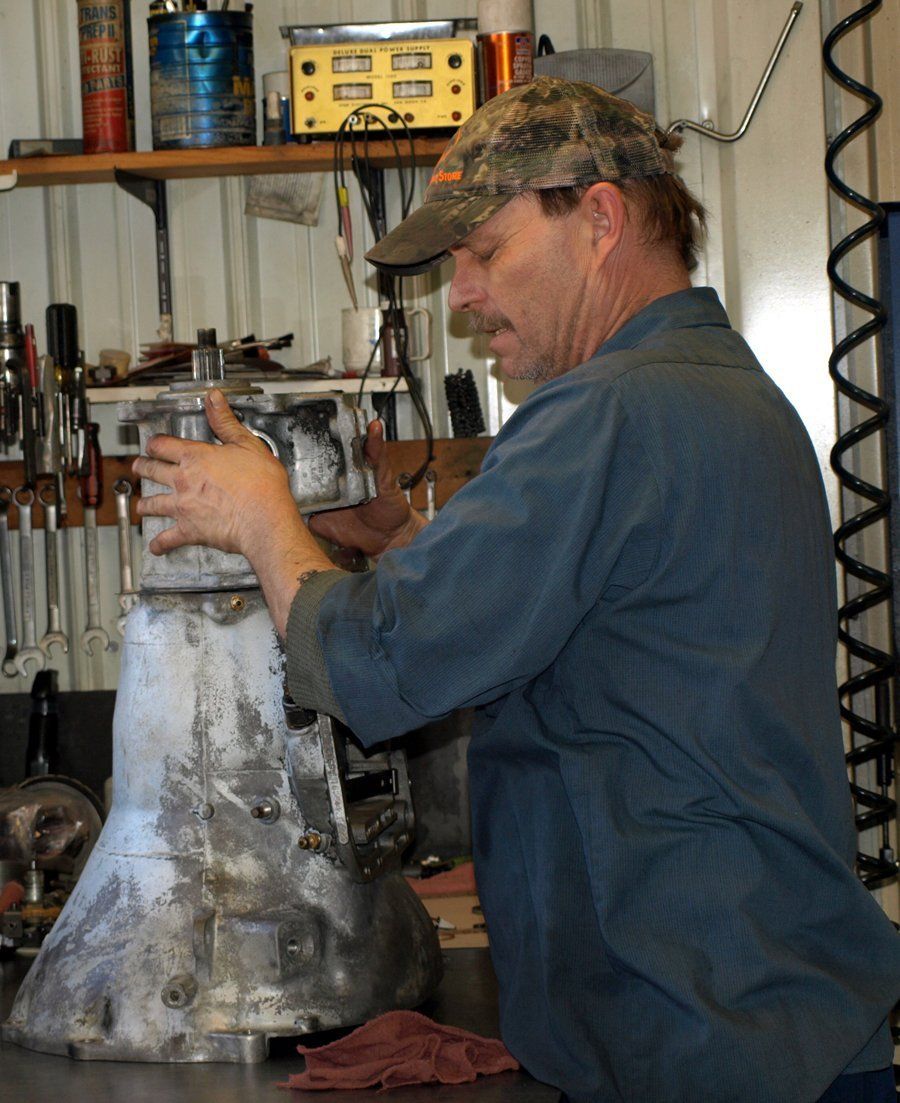 Man in a workshop holding a large metal vessel beside tools and shelves