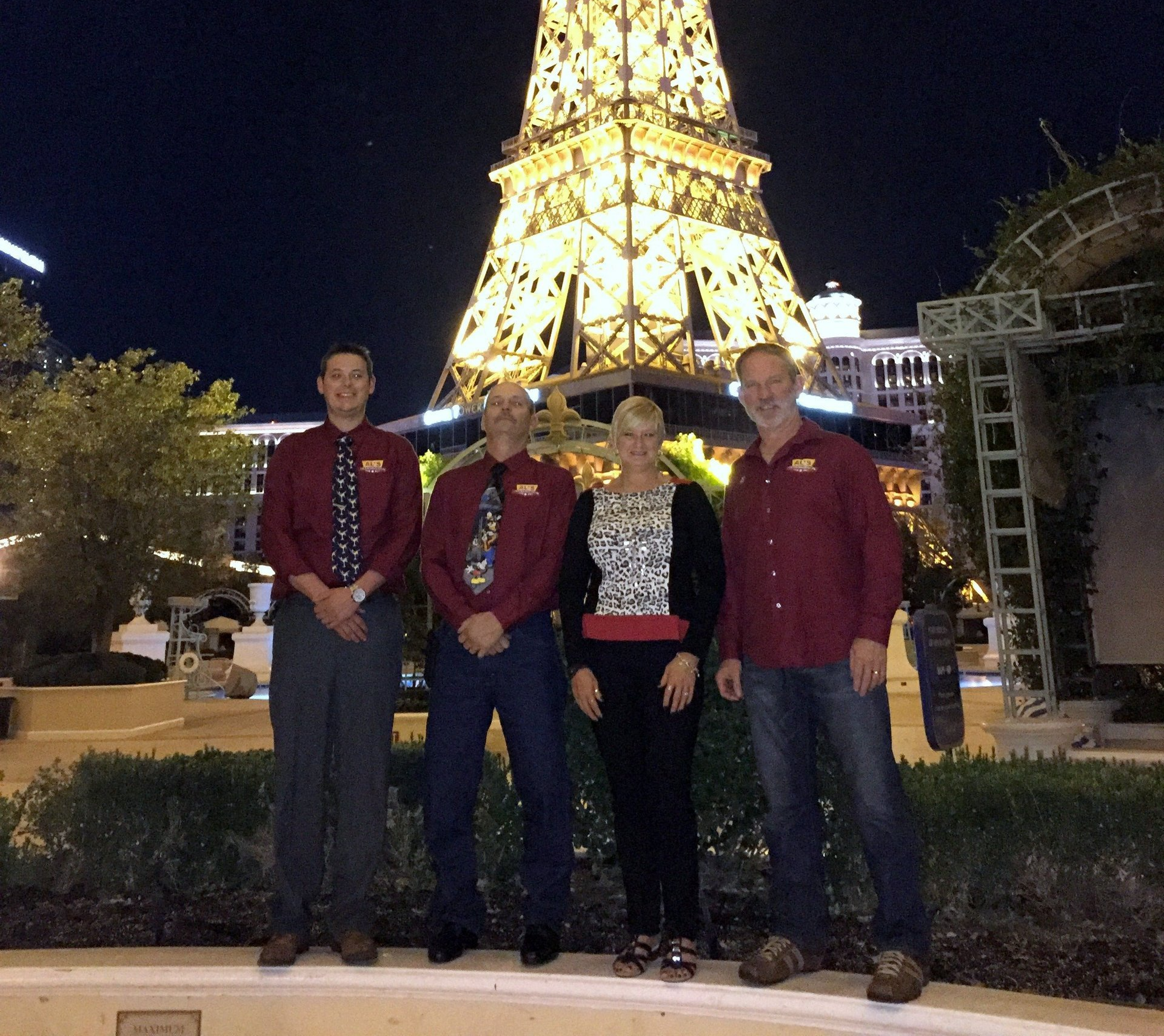 Four people standing at night in front of a lit Eiffel Tower replica