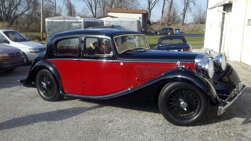 Classic black-and-red vintage car parked outdoors in a gravel lot.