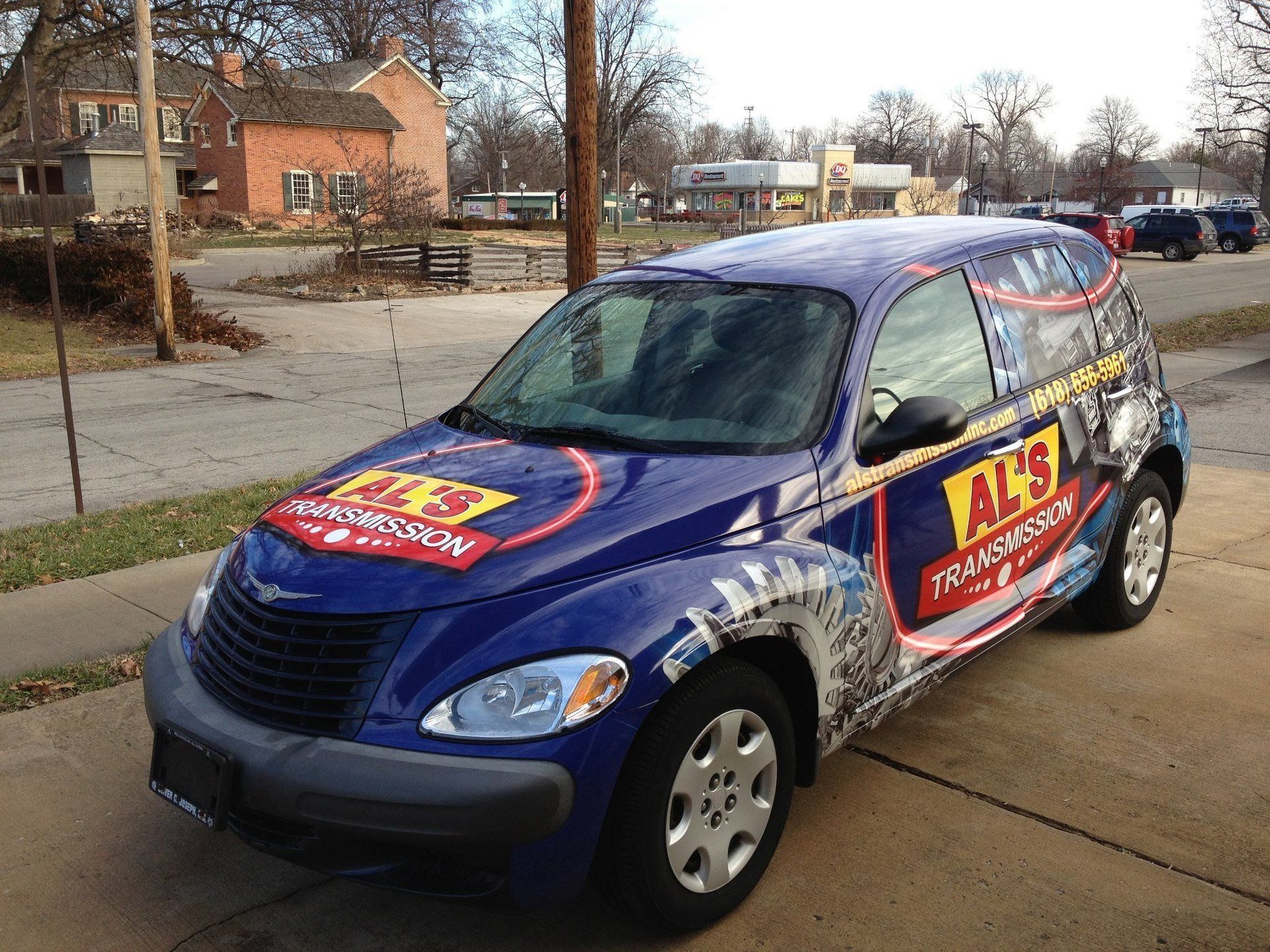 Blue promotional car with red-and-yellow ads parked on a sidewalk near houses