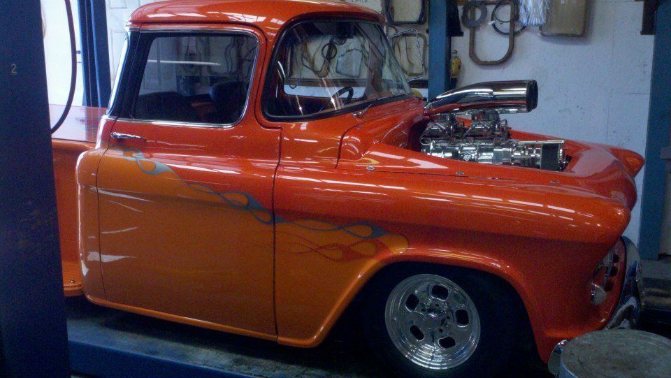 Bright orange vintage pickup truck indoors, viewed from the side with chrome details.