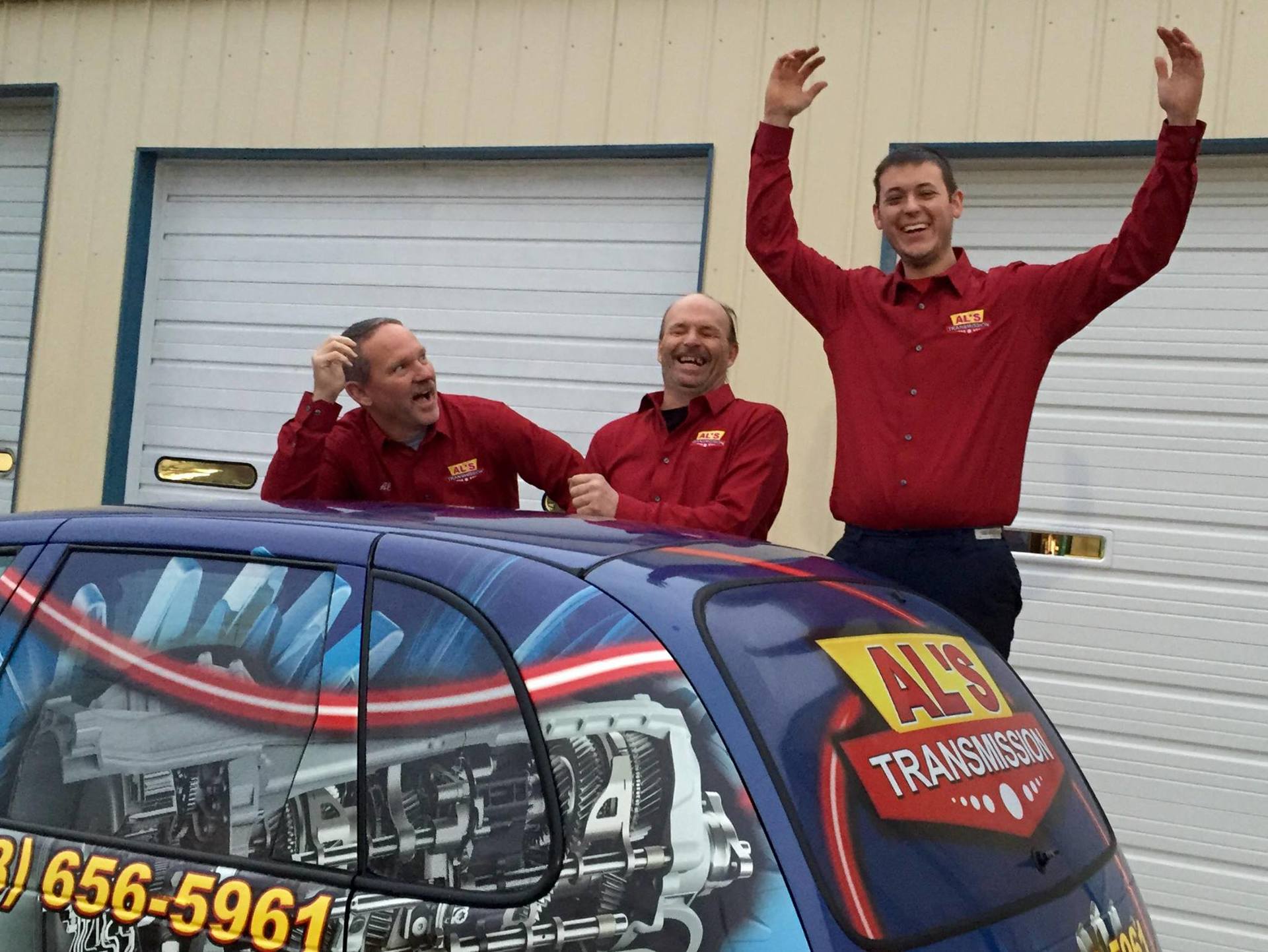 Three people in red shirts standing beside a branded service car, cheering in front of a garage.