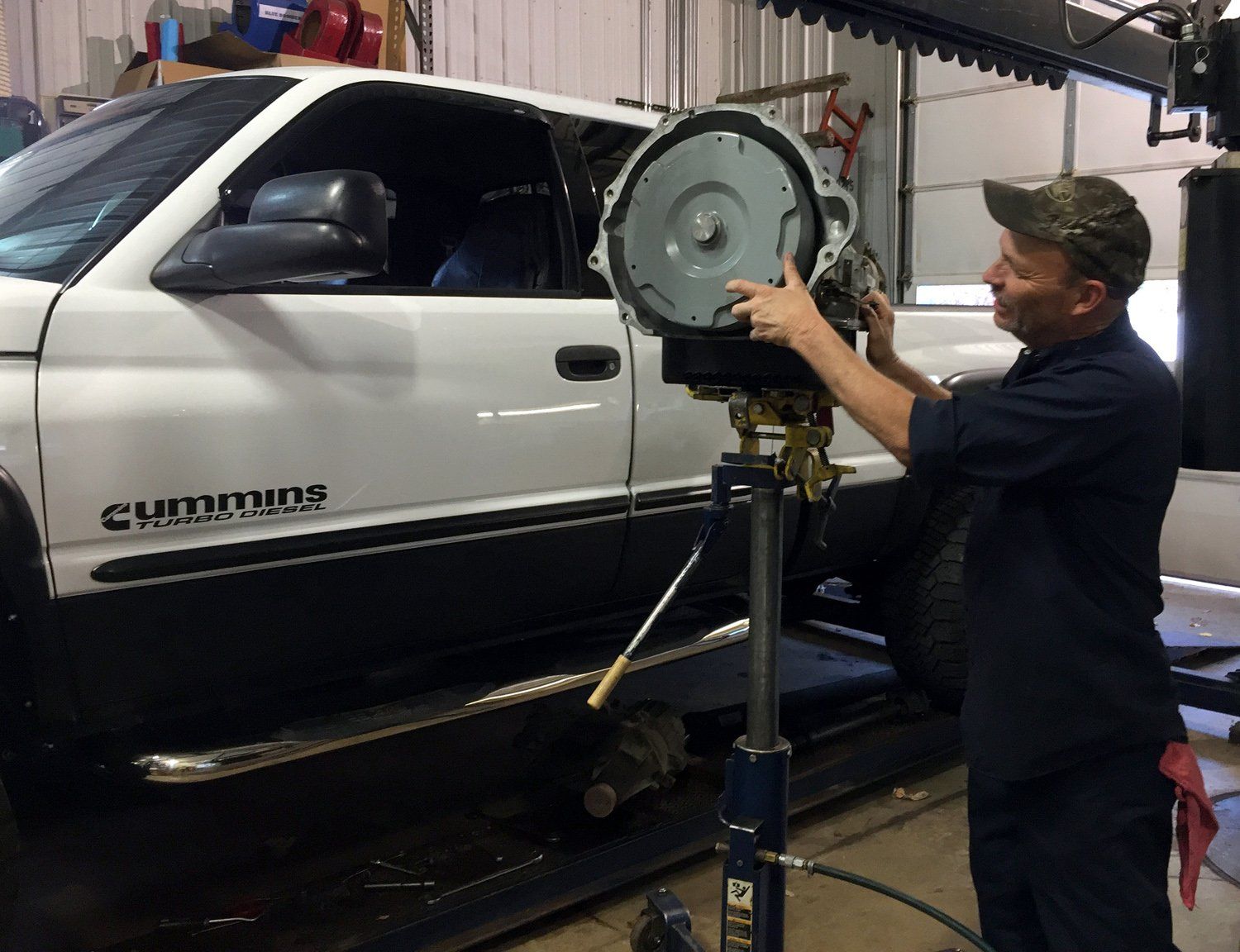 Mechanic using a tool to align a white Chevrolet truck wheel in a garage