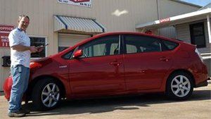 Red hatchback parked outside a storefront, with a man standing beside the driver’s door.